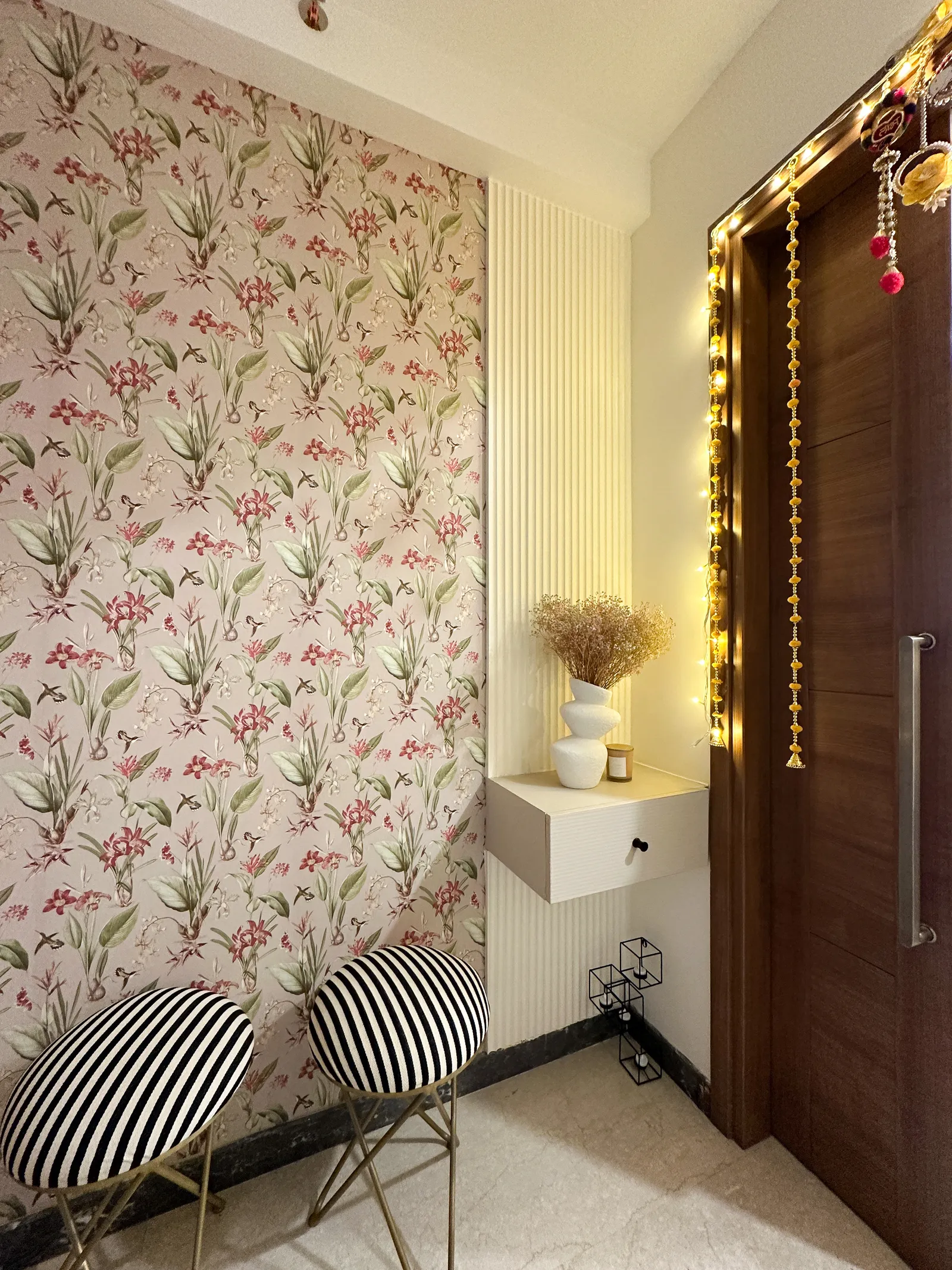 Foyer with floral wallpaper, wall shelf and fairy-light-lit door — Somani's Residence